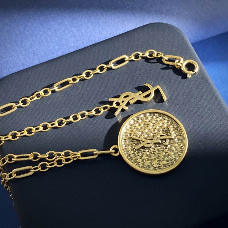 Saint Laurent YSL gold-tone coin pendant necklace with Cassandre charm on dark blue surface